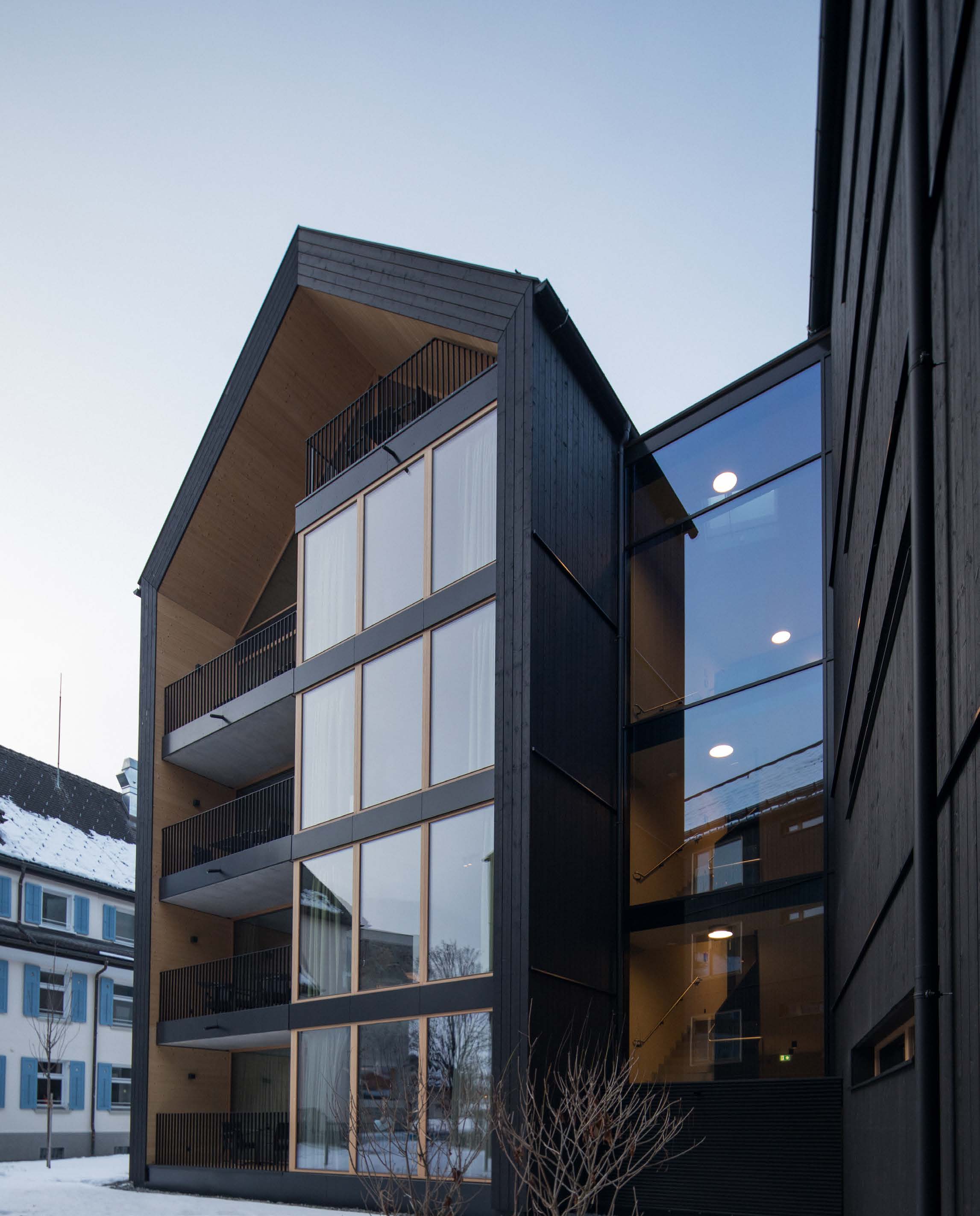 SUITES Montafon in winter, black timber facade with gable, balconies and glass front