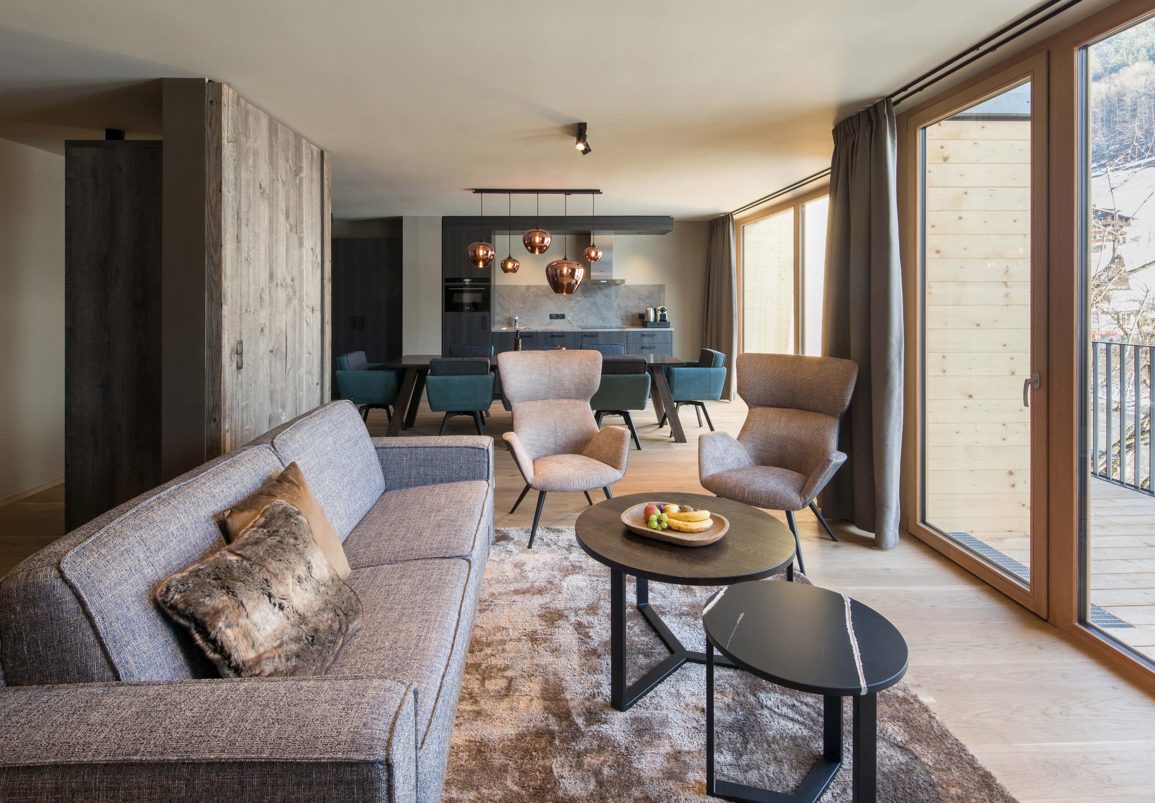 Living area of an apartment with sofa, armchairs, dining area and balcony door